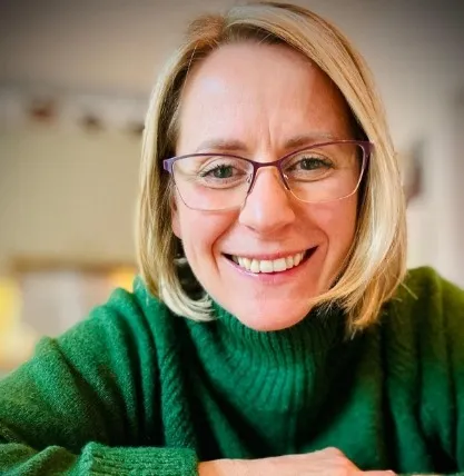Sally Varley smiling, wearing a green turtleneck sweater and glasses